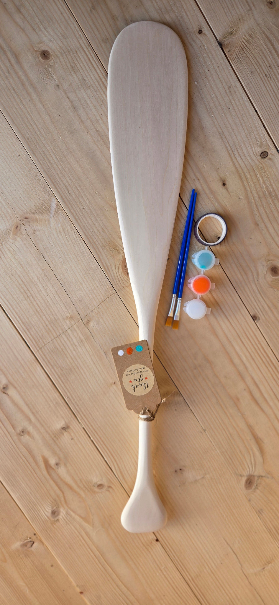 Wooden paddle with paint supplies on a wooden floor